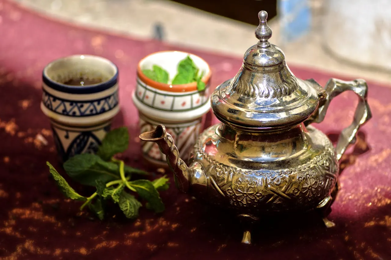 A steaming cup of traditional Moroccan mint tea being poured from a silver teapot