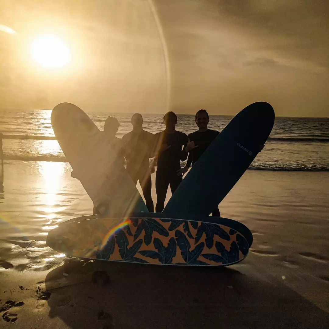Group of local and international surfers sharing waves at sunset with silhouettes against the orange sky