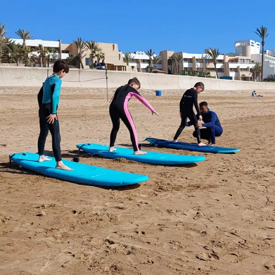 Surf instructor teaching a beginner how to surf on gentle waves at Agadir Beach with palm trees in background