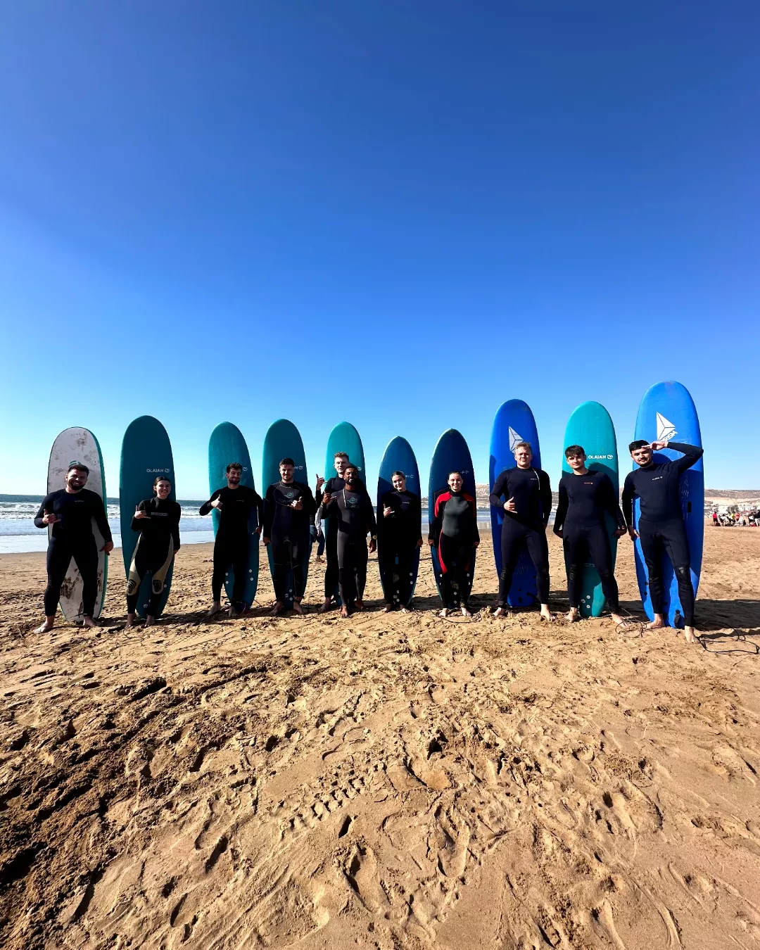 The surfers stand in a single line in front of their boards on the beach